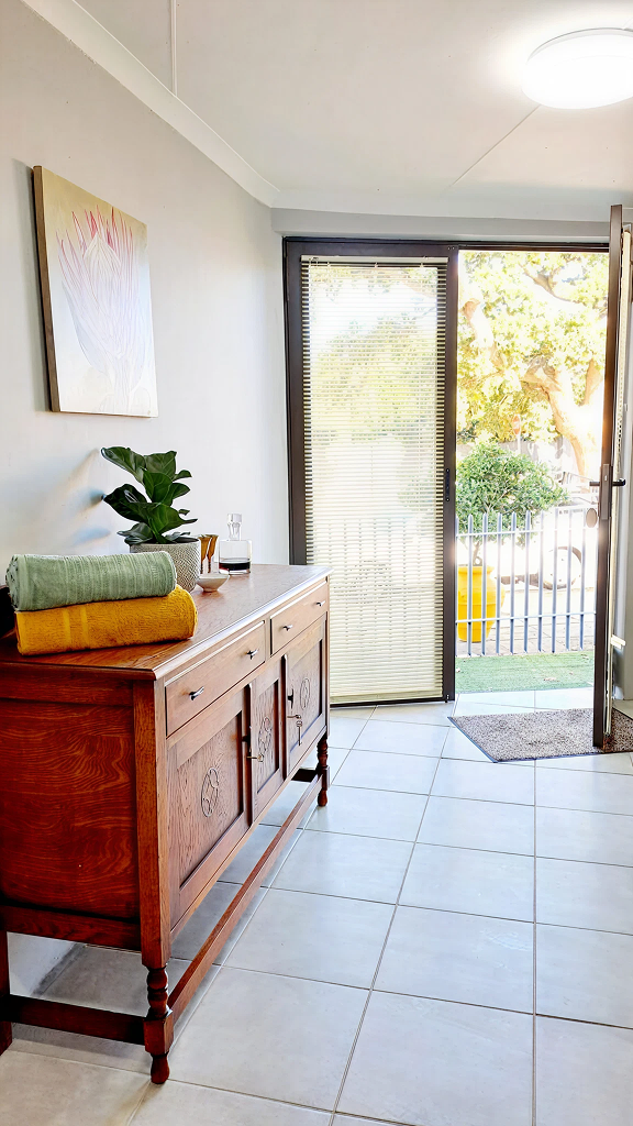 Bright guesthouse entrance with sliding door, wooden dresser and protea artwork